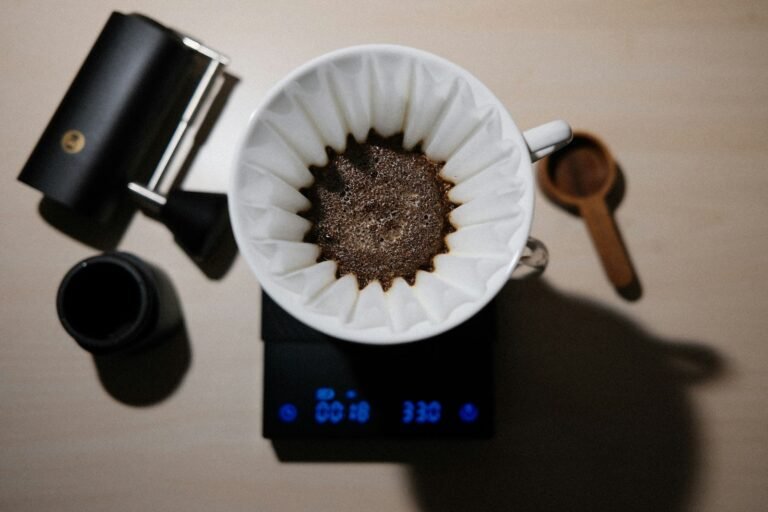 Café moulu dans un filtre papier posé sur une balance de précision, à côté d'un moulin manuel et d'une cuillère en bois