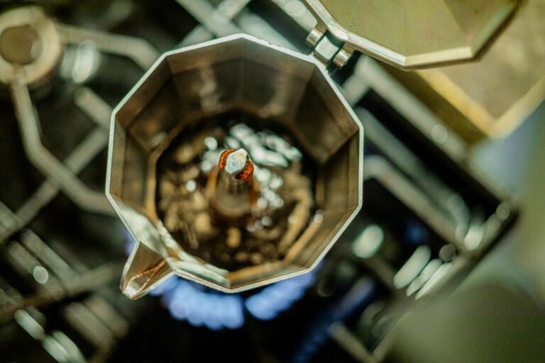 Cafetière italienne ouverte vue de dessus sur une flamme bleue, le café monte par la cheminée centrale