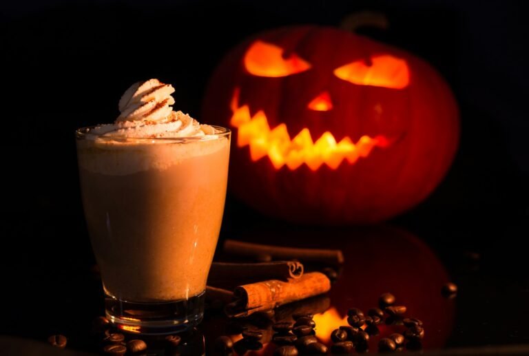 Latte épicé surmonté de chantilly, bâtons de cannelle et grains de café, citrouille sculptée illuminée au fond